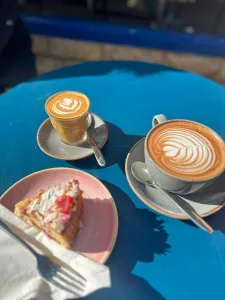 Two coffees and cake on a blue table in the sun